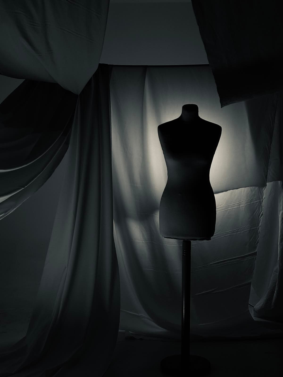 Black dress form lit against pale draped fabric